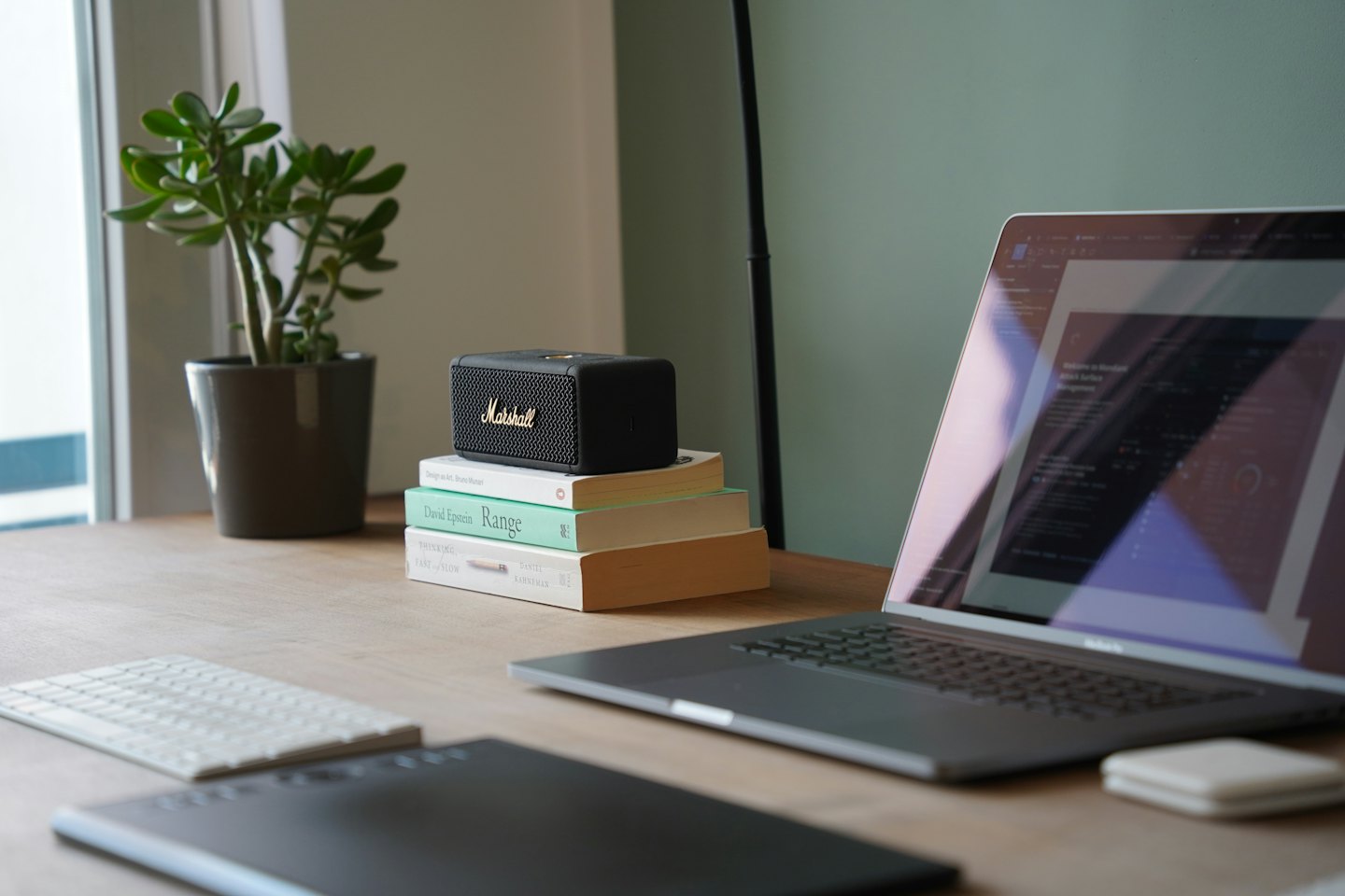 Laptop, boeken en luidspreker op een houten bureau.