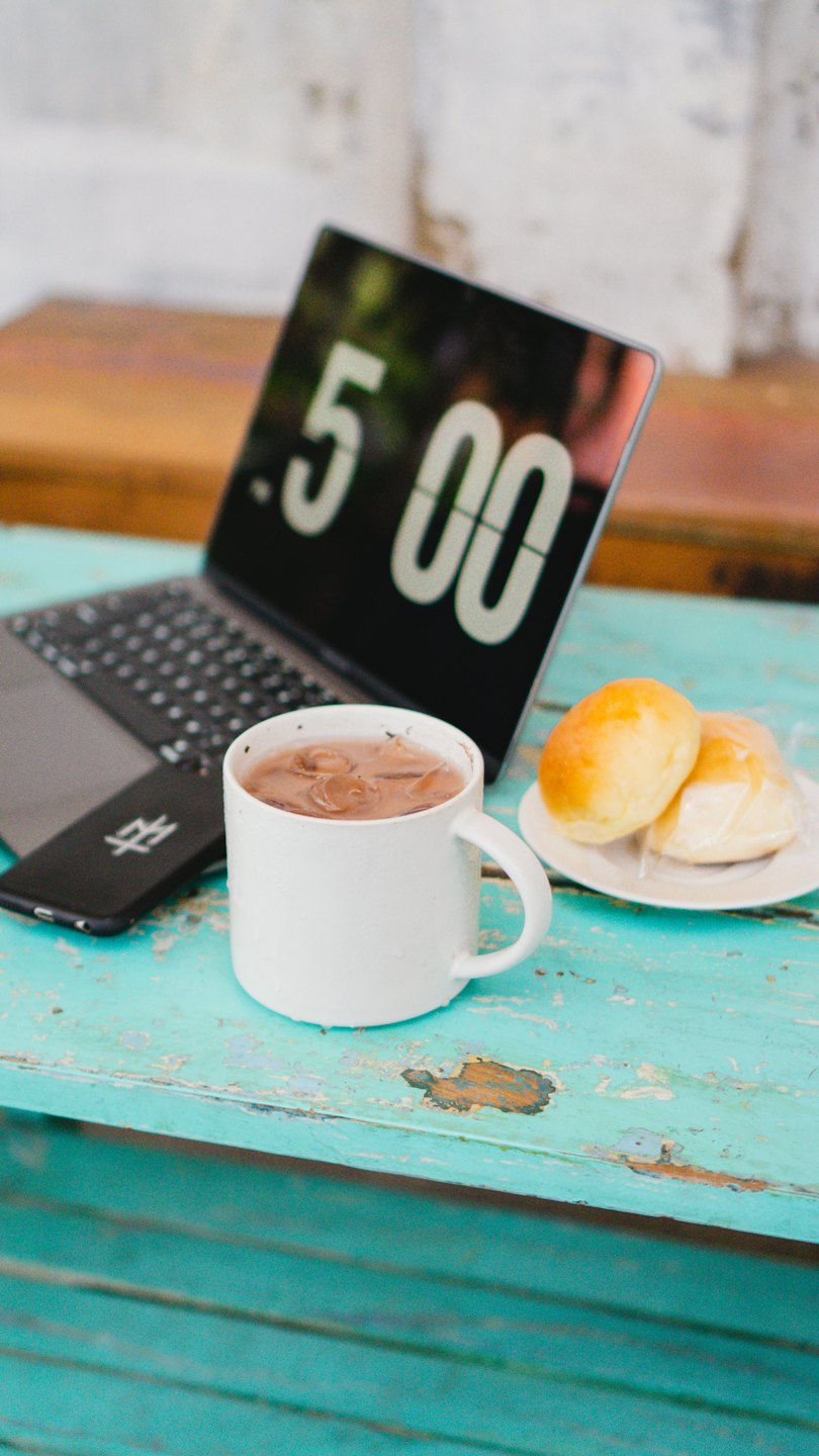 Laptop met koffie en gebak op tafel.